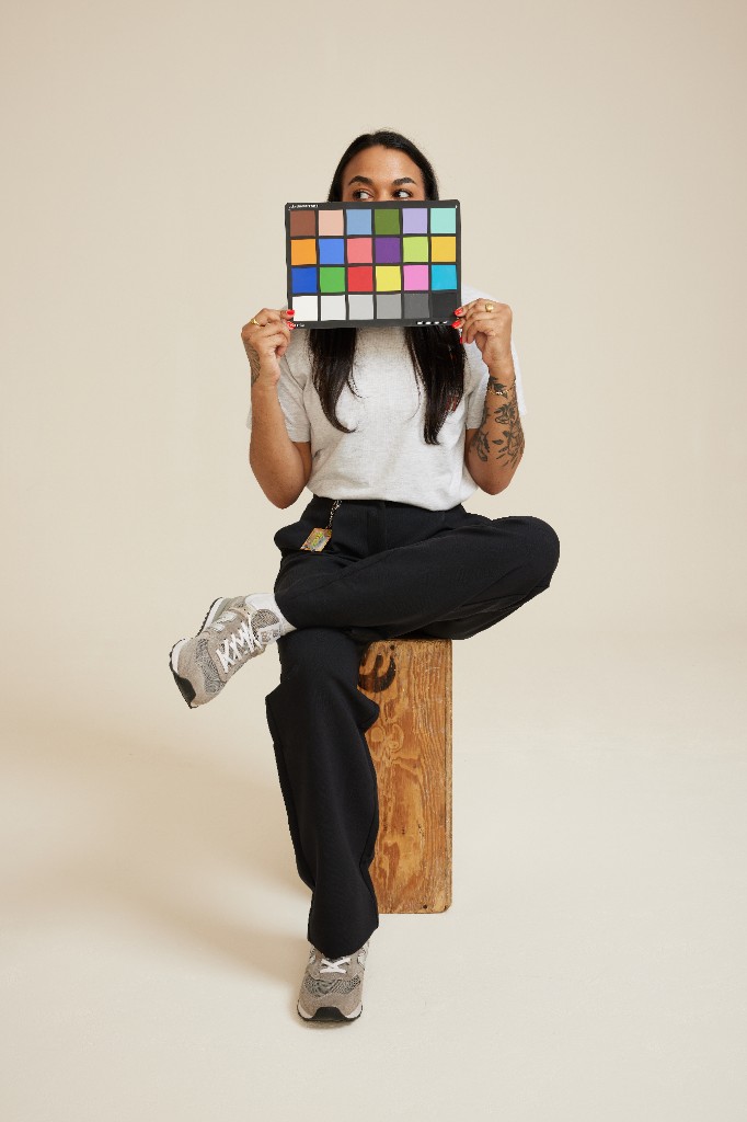 Sofia sitting on a wooden crate, holding a color checker card, with eyes peeking out playfully